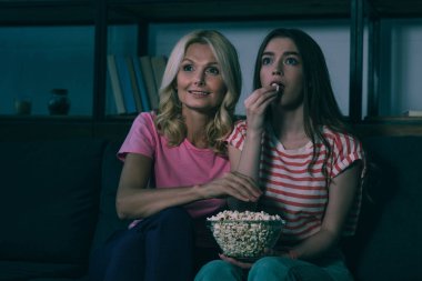 Dikkatli anne ve kız televizyon izliyor ve patlamış mısır yiyor. 