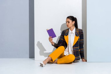 Beyaz ve gri üzerine mor bir kitap tutarken oturan çekici kız 