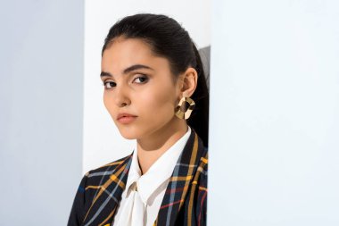 Güzel ve genç bir kadın beyaz ve gri kameraya bakıyor.