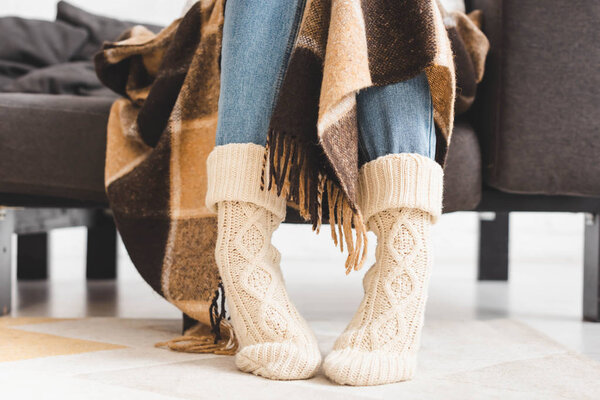cropped view of girl in knitted socks sitting in blanket on sofa 