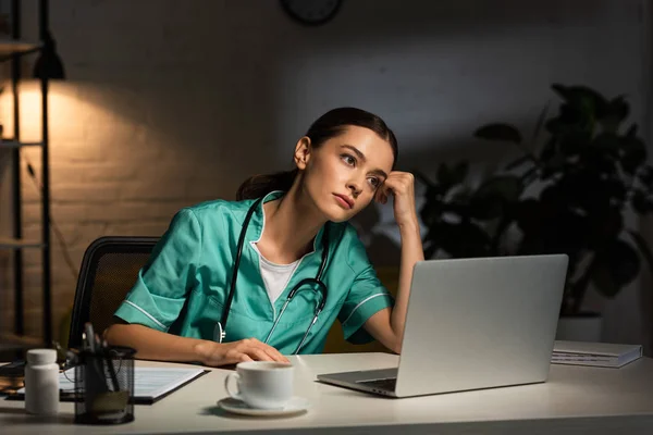 Attractive Tired Nurse Uniform Sitting Table Looking Away Night Shift — Stok fotoğraf