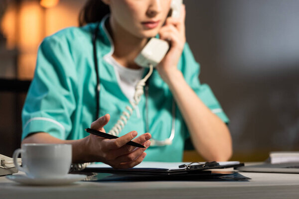 cropped view of nurse in uniform talking on telephone during night shift