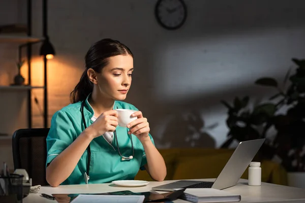 Enfermera Atractiva Uniforme Sentada Mesa Sosteniendo Taza Durante Turno Noche — Foto de Stock