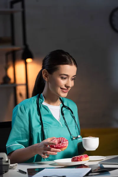 Χαμογελαστή Νοσοκόμα Στολή Κρατώντας Ντόνατ Και Κύπελλο Κατά Διάρκεια Της — Φωτογραφία Αρχείου