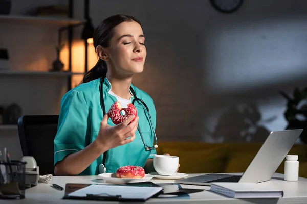 Enfermeira Atraente Uniforme Sentado Mesa Comer Donut Durante Turno Noite — Fotografia de Stock