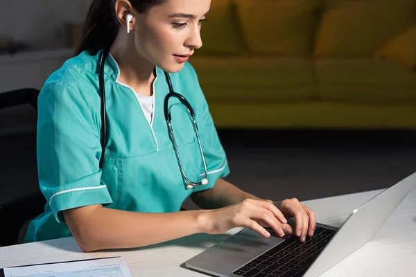 작업복을 매력적 간호사가 식탁에 앉아서 시간에 노트북을 사용하는 — 스톡 사진