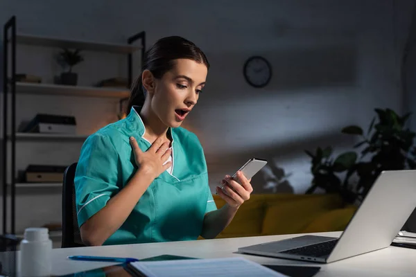 Infermiere Scioccato Uniforme Seduto Tavola Utilizzando Smartphone Durante Turno Notte — Foto Stock