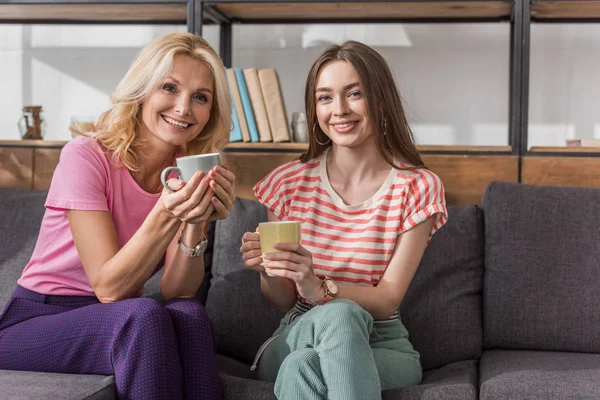 Cheerful Mother Daughter Looking Camera While Sitting Sofa Holding Tea — Stock Photo, Image