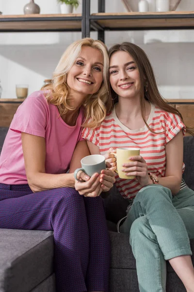 Feliz Madre Hija Mirando Cámara Mientras Están Sentadas Sofá Sosteniendo — Foto de Stock