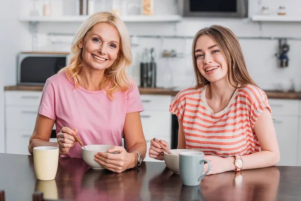 Feliz Madre Hija Mirando Cámara Mientras Están Sentadas Mesa Cocina — Foto de Stock