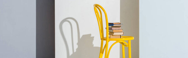 panoramic shot of yellow chair with books on white and grey 