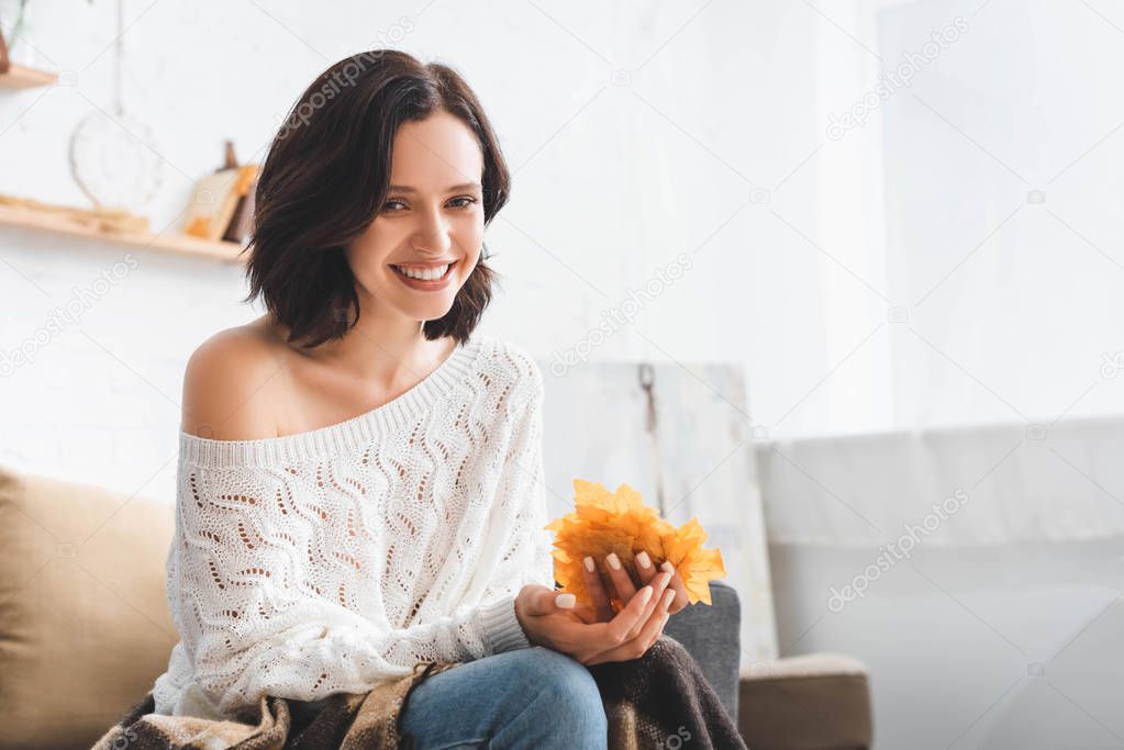 beautiful smiling woman holding yellow autumn leaves in living room