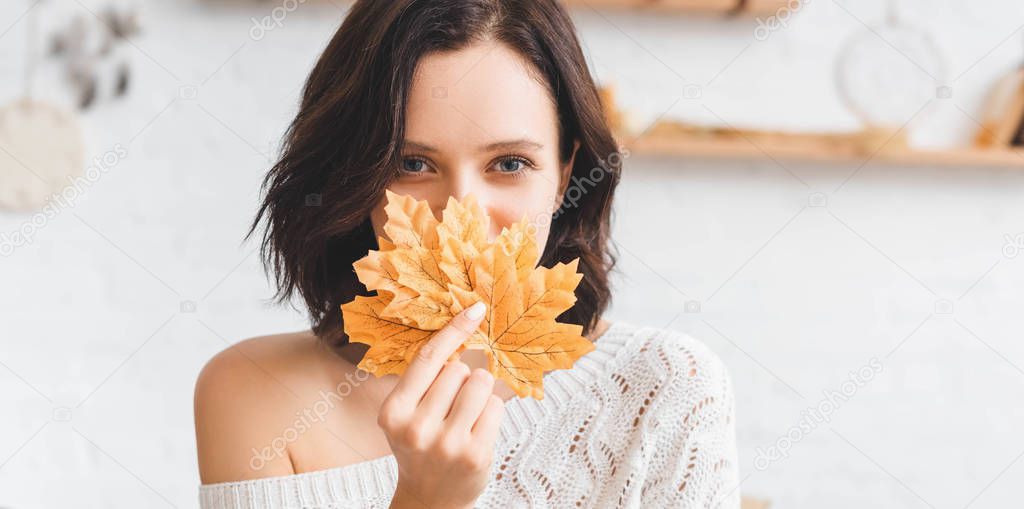 happy brunette girl holding yellow autumn leaves in front of face 