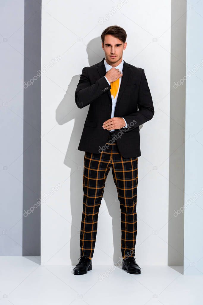 stylish man touching yellow tie on white and grey 