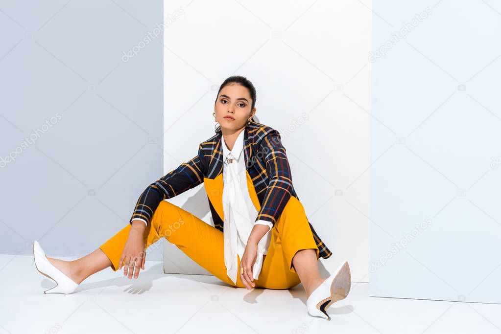 stylish girl looking at camera while posing on grey and white 