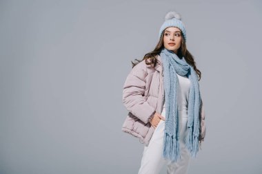 Güzel, şık bir kız, kalın bir palto, örgü şapka ve eşarp giyiyor, gri renkte izole edilmiş.