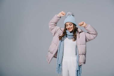 Çekici, mutlu bir kadın, örgü şapka ve atkıyla, gri renkte dans ediyor.