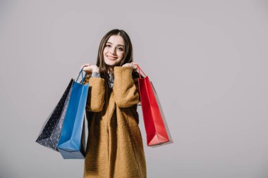 Gri renkte izole edilmiş bej ceketli, alışveriş torbaları taşıyan şık bir kız.