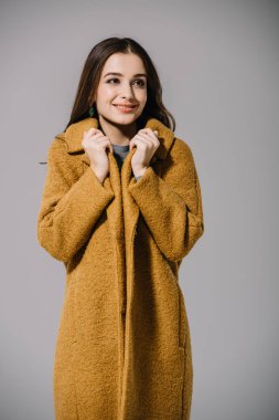 Gülümseyen soğuk kız, gri üzerine izole edilmiş, bej ceketli.