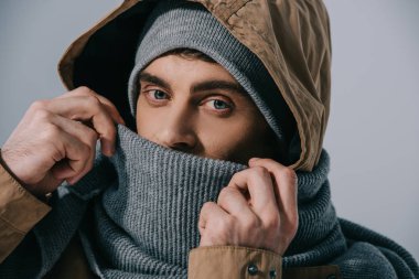 Şapka, eşarp ve başlık takan yakışıklı genç adam, gri renkte izole edilmiş.