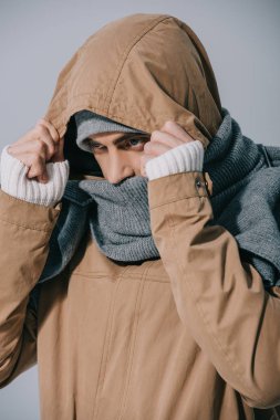 Şapka, eşarp ve başlık takan genç adam, gri renkte izole edilmiş.