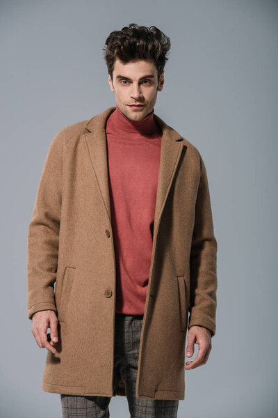 модный мужчина, позирующий в модном бежевом пальто, изолированный на сером
