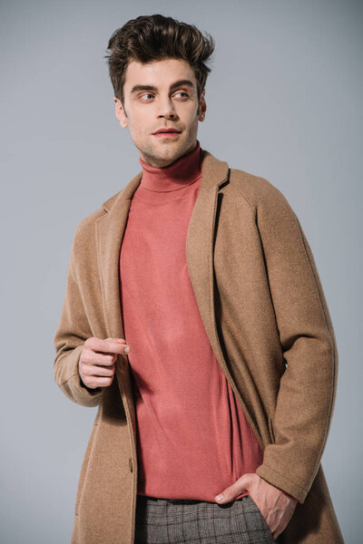 стильный мужчина позирует в бежевом пальто, изолированный на сером
