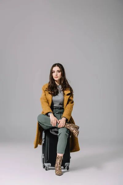 Schöne Stilvolle Mädchen Beigen Mantel Sitzt Auf Reisetasche Auf Grau — Stockfoto