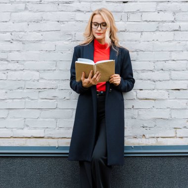 Siyah ceketli, gözlüklü, kitap okuyan çekici bir iş kadını. 