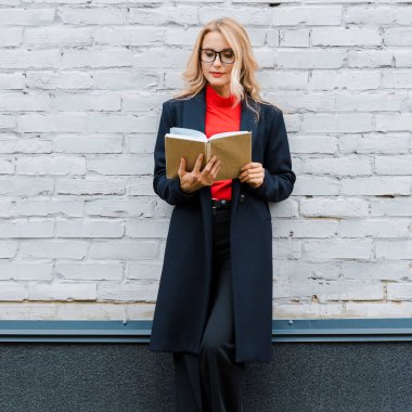 attractive businesswoman in black coat and glasses reading book  clipart