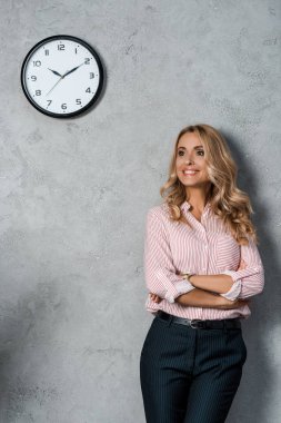 Kollarını kavuşturup gülümseyen ve başka tarafa bakan çekici bir iş kadını. 