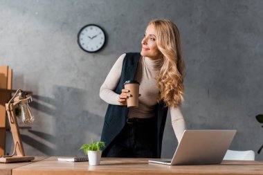 attractive and smiling businesswoman holding paper cup and looking away  clipart