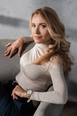  Çekici ve sarışın iş kadını kameraya bakıyor ve koltukta oturuyor. 