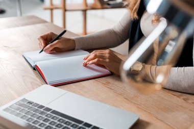 Masada oturan sarışın iş kadınının ofis defterine yazı yazması. 