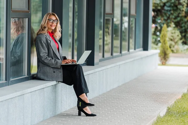 Atractiva Mujer Negocios Abrigo Gafas Sonriendo Sosteniendo Portátil —  Fotos de Stock