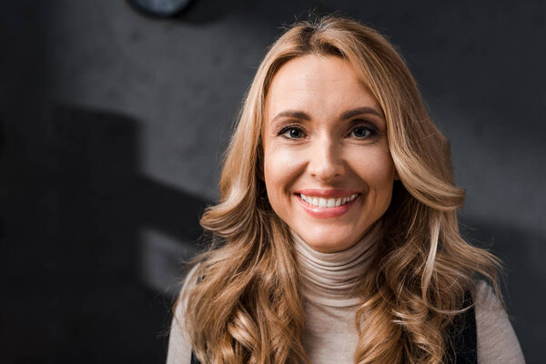 attractive and blonde businesswoman smiling and looking at camera in office 