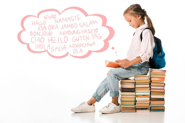 cheerful schoolkid sitting on books and reading near greeting letters on white 