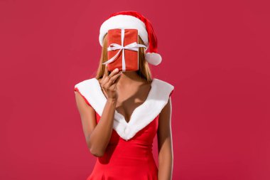 Noel Baba şapkalı ve noel elbiseli genç Afrikalı Amerikalı kız kırmızı kutunun arkasında saklanıyor.