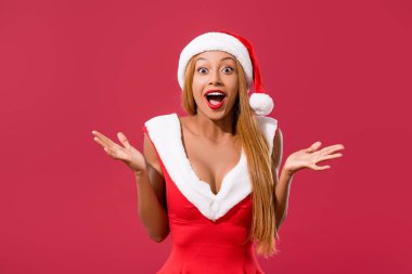 Noel Baba şapkası ve Noel elbisesi giymiş Aftrikalı Amerikalı kız kırmızı üzerine izole edilmiş bir jest gösteriyor.