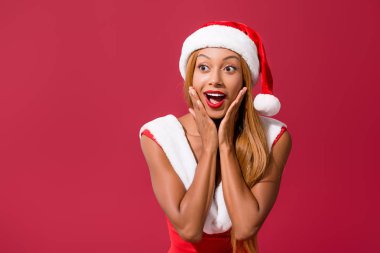 Noel Baba şapkası ve noel elbisesi giymiş Afro-Amerikalı bir kız kırmızı ışıkta izole bir şekilde gözlerini kaçırıyor.