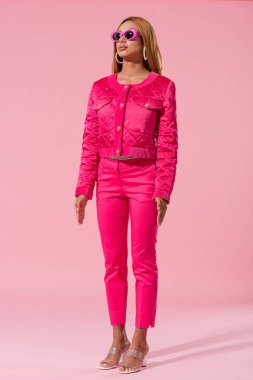 Güneş gözlüklü modacı Afro-Amerikan kadın pembe arka planda duruyor, oyuncak bebek konsepti