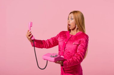 Şok olmuş, modaya uyan Afro-Amerikan kadın telefonuna bakıyor pembe, moda bebeği konseptine izole edilmiş.