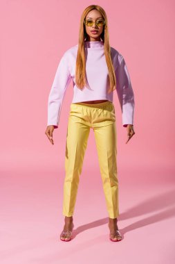 Pembe arka planda duran şık, sarışın Afrikalı Amerikalı kadın, moda bebeği konsepti