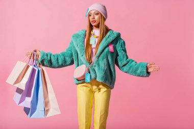 Düşünceli, şık Afrikalı Amerikalı kadın alışveriş çantalarını pembe, moda bebeği konseptine izole etmiş.
