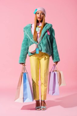Çekici, şık Afrikalı Amerikalı kadın pembe arka planda alışveriş torbaları tutuyor, oyuncak bebek konsepti