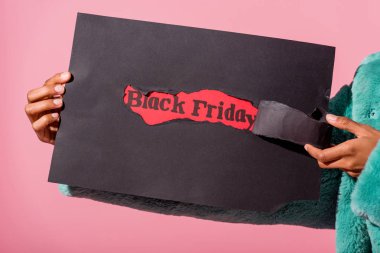 partial view of african american woman holding black torn paper with black friday inscription isolated on pink clipart