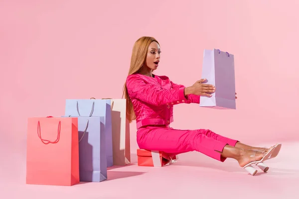非洲女人坐在礼品盒上 拿着粉色背景的购物袋 这是一种时尚娃娃的概念 — 图库照片