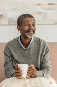 mosolygó afro-amerikai férfi ül takaróval a térdén, és kezében csésze melegítő ital