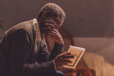 senior, depressed african american man looking at photo frame clipart