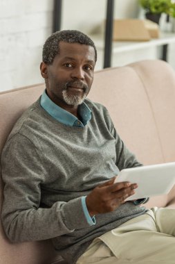 Ciddi bir Afrikalı Amerikalı dijital tablet tutuyor ve kameraya bakıyor.